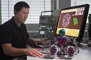 Der Ingenieur Philipp Mittendorfer (TU München) mit dem Roboter Bioloid, der 31 sechseckige Sensormodule verteilt über den ganzen Körper besitzt. Die Sensormodule messen Temperatur, Berührung und Beschleunigung, ähnlich wie die menschliche Haut. Foto: Andreas Heddergott / TU München